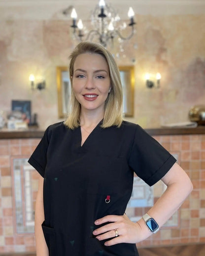 Woman in black scrub top standing in a room with a chandelier and wall lights.