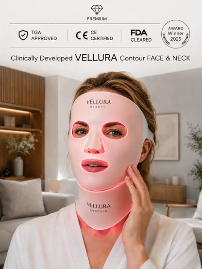 A woman wearing a glowing pink Vellura Contour Face & Neck mask in a bright, modern living room setting. The image includes marketing badges at the top for TGA Approved, CE Certified, FDA Cleared, and Award Winner 2025.
