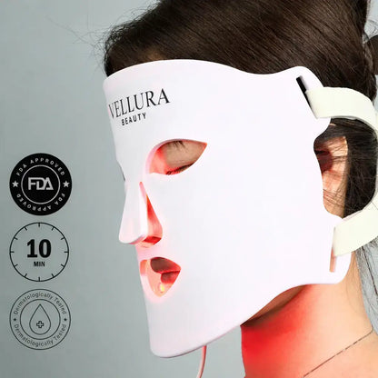 Woman wearing a Vellura Beauty face mask with visible red light on a gray background